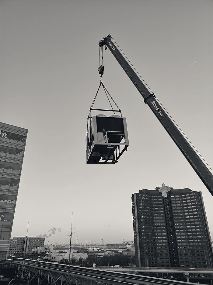 Een koelmachine hangt aan de kraan boven de Rotterdamse skyline