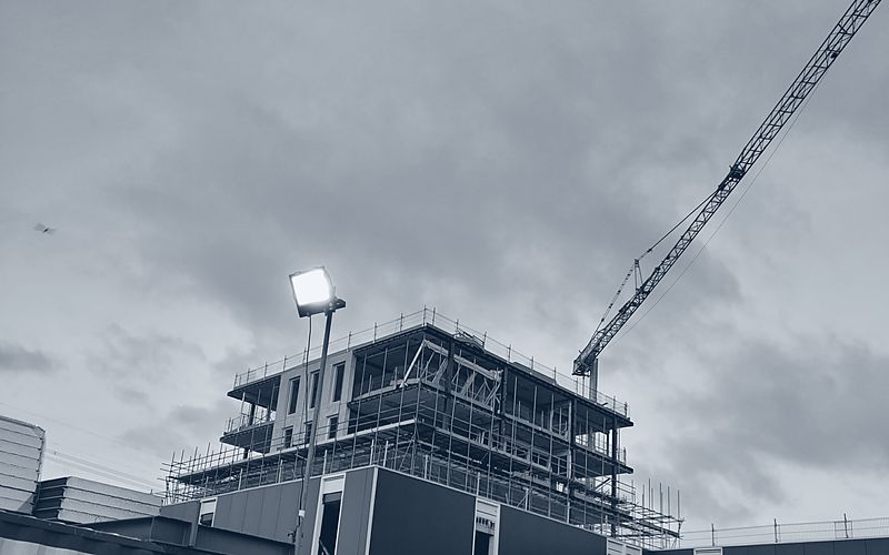 Ruwbouw van een utiliteitsgebouw met steiger en torenkraan bij schemer